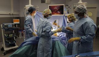 Surgeon Lara Ribeiro Parenti, second left, holds a surgical instrument during the surgery of Caroline Erganian at Bichat Hospital, AP-HP, in Paris, Wednesday, Dec. 2, 2020. Erganian, 58, hopes to shed more than a third of her weight as a result of having a large part of her stomach cut out and be free of knee and back pain — and of her cane. She prayed in the final weeks that her phone wouldn&#x27;t ring with news of another delay.  (AP Photo/Francois Mori)