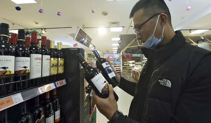A man wearing a face mask compares two bottles of Australian wine at a supermarket in Hangzhou in east China&#39;s Zhejiang province on Nov. 27, 2020. China&#39;s government on Thursday, Dec. 10, 2020 slapped more taxes on wine from Australia, stepping up pressure in a bitter diplomatic conflict over the coronavirus, territorial disputes and other irritants. (Chinatopix via AP)