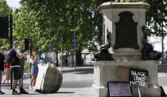 FILE - In this file photo dated Monday, June 8, 2020, people look at the empty pedestal after a statue of notorious slave trader Edward Colston was pulled down during a Black Lives Matter demo, in Bristol, England.     Four people have been were charged with criminal damage over the toppling of the 17th-century slave trader  Colston statue, according to an announcement Wednesday Dec. 9, 2020, by Britain’s Crown Prosecution Service.  (AP Photo/Kirsty Wigglesworth, FILE)