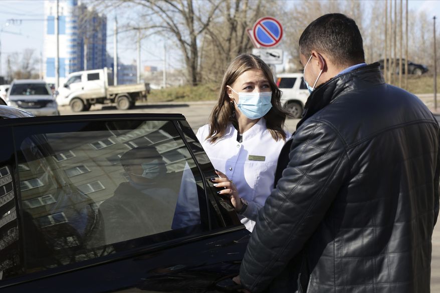 Vadim Kostenko opens the car door for Dr. Veronica Arzhadeyeva in Irkutsk, Russia, Friday, Oct. 23, 2020, as she leave the car to visit a patient. As the resurgence of the coronavirus outbreak hit Russia this fall, one of the most common complaints from people with virus symptoms who are self-isolating at home and are supposed to call a visiting doctor service has been waiting days for anyone to arrive. A group of volunteers came to the rescue, offering a simple service of driving medical workers to their house visits. Vadim Kostenko, a 37-year-old entrepreneur came up with the initiative. (AP Photo/Alexander Novikov)