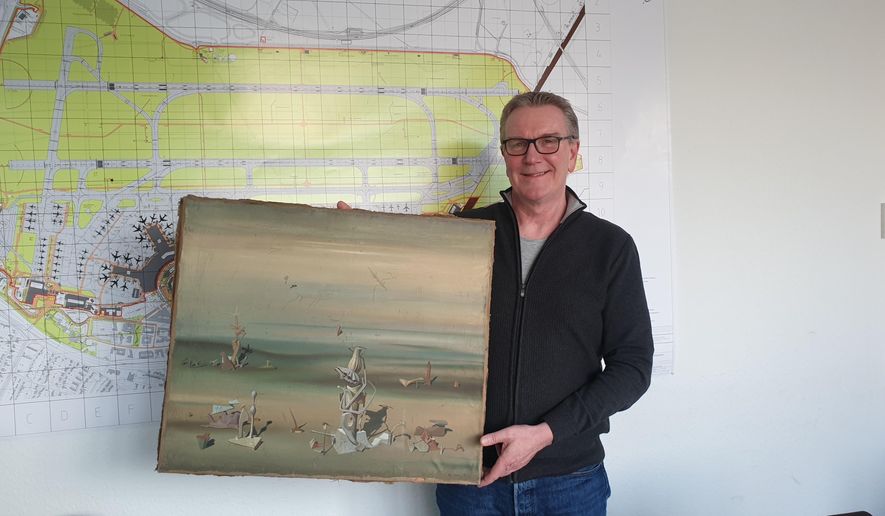 In this photo released by the police department in Duesseldorf on Thursday Dec. 10, 2020, showing Chief Detective Michael Dietz holding a painting from French artist Yves Tanguy.  A businessman, whose identity was not given, boarded a flight from Duesseldorf to Tel Aviv on Nov. 27, but forgot the painting by French surrealist Yves Tanguy, which was wrapped in cardboard, on the check-in counter. By the time he landed in Israel and contacted Duesseldorf police, the 280,000 Euro, (dollar 340,000), oeuvre had disappeared but was later found at a nearby paper dumpster, Duesseldorf police said. (Polizei Duesseldorf via AP)