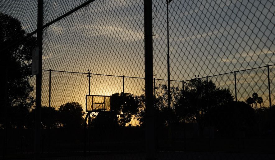 The sun sets behind a basketball backboard in a park temporarily closed due to COVID-19 in Commerce, Calif., Wednesday, Dec. 9, 2020. Thirteen counties in Northern California will be placed under the state's most restrictive coronavirus rules this week because capacity in intensive care units has fallen below 15%, and officials warned Wednesday that hospitals across the state are filling up with COVID-19 patients. (AP Photo/Jae C. Hong)