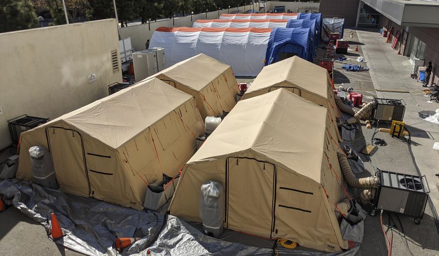 FILE - In this Monday, March 30, 2020, file photo, triage tents are deployed for a possible surge of emergency COVID-19 patients outside of the Los Angeles County + USC Medical Center in Los Angeles. A health official in California's third largest county is urging hospitals to cancel elective surgeries and implement plans for an onslaught of COVID-19 patients, as intensive care units fill up statewide amid spiking virus cases. Dr. Carl Schultz says ambulances have been waiting for hours to unload patients because Orange County emergency rooms are so backed up. (AP Photo/Damian Dovarganes, File)