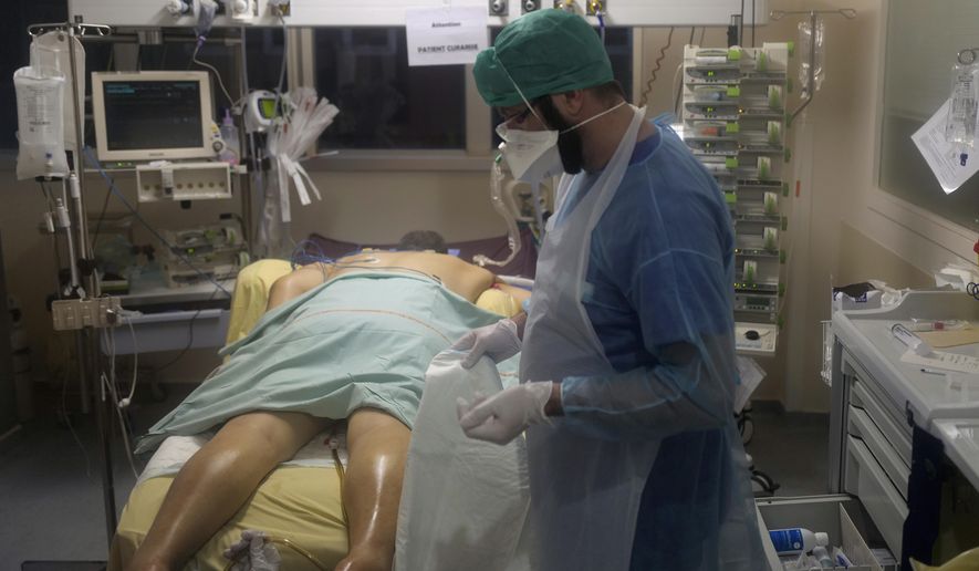 Paramedic Bertrand Brissaud, cares for the patient in room No. 10, a few hours before he died after his nearly month-long battle against COVID-19 at Bichat Hospital, AP-HP, in Paris Tuesday, Dec. 1, 2020. The patient in room No. 10 died later on Dec. 1. His was one of 775 virus deaths in France that day, adding to a national death toll now topping 56,000 and the worldwide count of more than 1.5 million dead. As one of the man's carers, Brissaud had been more physically intimate with him than many people are with their friends. (AP Photo/Francois Mori)