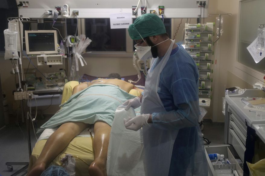 Paramedic Bertrand Brissaud, cares for the patient in room No. 10, a few hours before he died after his nearly month-long battle against COVID-19 at Bichat Hospital, AP-HP, in Paris Tuesday, Dec. 1, 2020. The patient in room No. 10 died later on Dec. 1. His was one of 775 virus deaths in France that day, adding to a national death toll now topping 56,000 and the worldwide count of more than 1.5 million dead. As one of the man's carers, Brissaud had been more physically intimate with him than many people are with their friends. (AP Photo/Francois Mori)