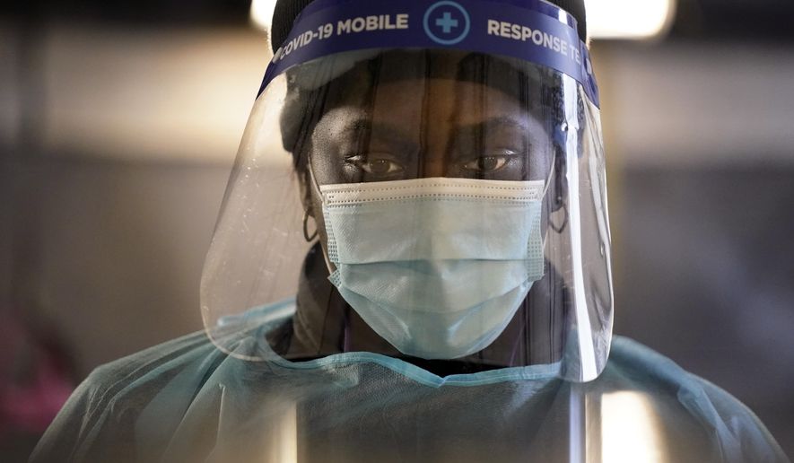FILE - In this Dec. 8, 2020, file photo, a health care worker wears personal protective equipment as she speaks to a patient at a mobile testing location for COVID-19 in Auburn, Maine. Doctors and nurses around the U.S. are becoming exhausted and demoralized as they struggle to cope with a record-breaking surge of COVID-19 patients that is swamping hospitals and prompting governors to clamp back down to contain the virus. (AP Photo/Robert F. Bukaty, File)