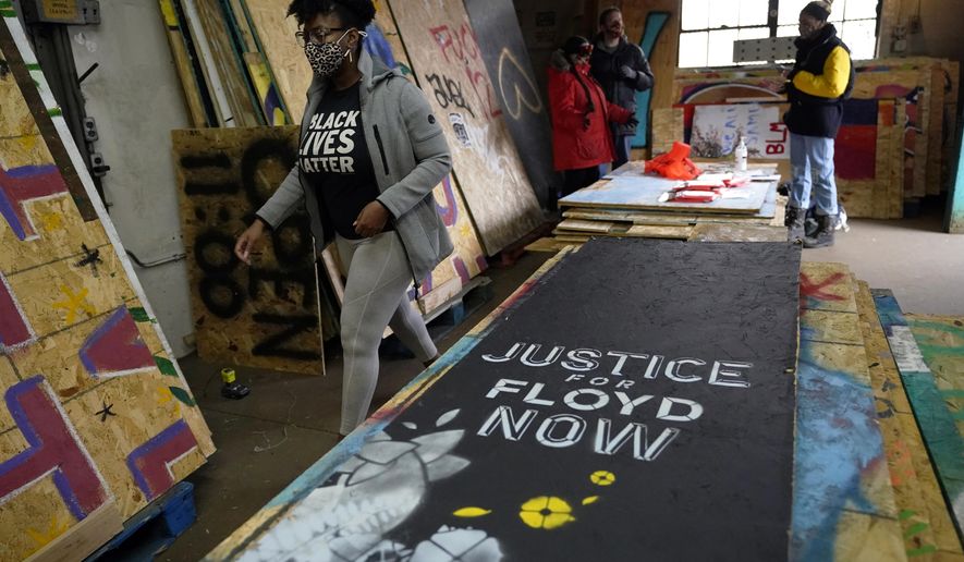 Leesa Kelly, left, walks past plywood mural boards as she and Kenda Zellner-Smith, background right, and volunteers meet at a warehouse, Saturday, Dec. 12, 2020, in Minneapolis to organize them. The two women formed the Save the Boards to Memorialize the Movement to preserve the painted expressions and pain born of outrage after the death of George Floyd at the hands of Minneapolis police in May. (AP Photo/Jim Mone)