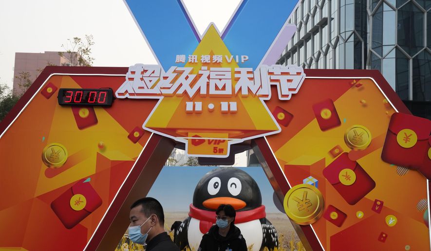 Workers wearing masks stand near a promotional booth for Tencent video in Beijing on Nov. 11, 2020. China&#39;s market regulator on Monday, Dec. 14, 2020 said it fined Alibaba Group and a Tencent Holdings-backed company for failing to seek approval before proceeding with some acquisitions. It also is launching a review of a merger of two online streaming platforms in the latest tightening of controls over the internet sector. (AP Photo/Ng Han Guan)