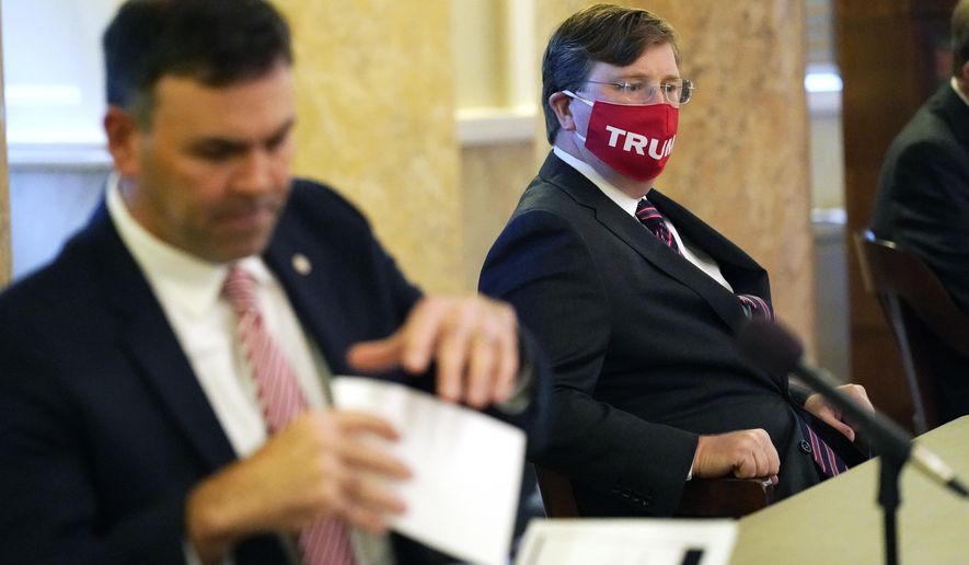 Republican Gov. Tate Reeves, right, an ardent supporter of President Donald Trump, wears his "Trump" face mask as he waits while Secretary of State Michael Watson tends to the official duties overseeing the casting of votes in Mississippi's Electoral College, at the state Capitol in Jackson, Monday, Dec. 14, 2020. (AP Photo/Rogelio V. Solis)