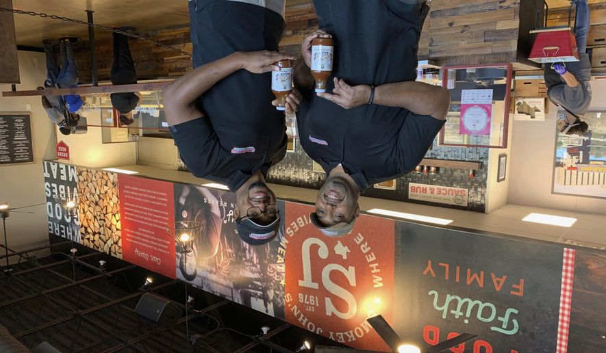 Juan Reeves, VP of Smokey John&#39;s BBQ, left, and his brother Brent Reeves, President of Smokey&#39;s John&#39;s BBQ, hold bottles of their famous barbecue sauce, which is available by mail order, at Smokey John&#39;s BBQ in Dallas on Dec. 10, 2020. (Jordyn Courtney/Smokey John&#39;s via AP)