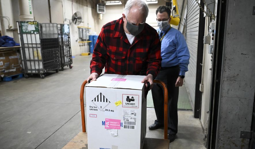 Minnesota Gov. Tim Walz lifts a just-delivered box of doses of the Pfizer-BioNTech COVID-19 vaccine, to get a sense of its weight, in the Minneapolis VA Hospital&#39;s loading dock Monday, Dec. 14, 2020. (Aaron Lavinsky/Star Tribune via AP, Pool)