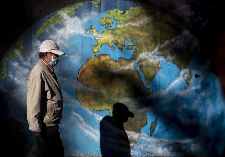 A man wearing a mask walks past graffiti depicting a globe in the Orcasitas neighborhood in Madrid, Spain, Monday, Sept. 28, 2020. Journalists from The Associated Press around the world assessed how the countries where they are posted have weathered the pandemic — and where those countries stand on the cusp of year two of the contagion. (AP Photo/Manu Fernandez)