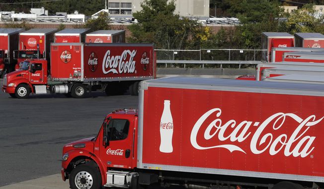 In this Oct. 14, 2019 photo a truck with the Coca-Cola logo, behind left, maneuvers in a parking lot at a bottling plant in Needham, Mass. The Coca-Cola Co. said Thursday, Dec. 17, 2020, it’s laying off 2,200 workers, or 17% of its global workforce, as part of a larger restructuring aimed at paring down its business units and brands. (AP Photo/Steven Senne, File)  **FILE**