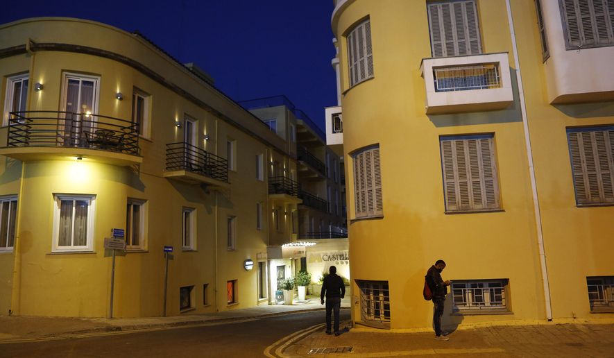 A man, right, uses his cell phone as another walks through the medieval core of central capital Nicosia, Cyprus, Friday, Dec. 11, 2020. Cyprus' Health Minister Constantinos Ioannou said that an island-wide night time curfew would be extended through December while bars, restaurants and shopping malls would be shut, high school students would stay at home for online classes and church services would be without worshippers amid concerns that a sustained spike in coronavirus infections hasn't receded despite restrictions. (AP Photo/Petros Karadjias)