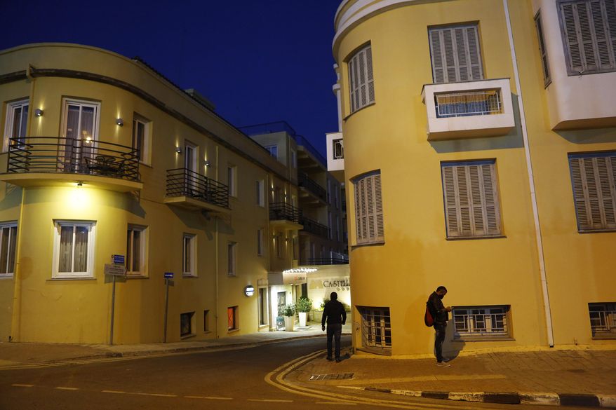 A man, right, uses his cell phone as another walks through the medieval core of central capital Nicosia, Cyprus, Friday, Dec. 11, 2020. Cyprus' Health Minister Constantinos Ioannou said that an island-wide night time curfew would be extended through December while bars, restaurants and shopping malls would be shut, high school students would stay at home for online classes and church services would be without worshippers amid concerns that a sustained spike in coronavirus infections hasn't receded despite restrictions. (AP Photo/Petros Karadjias)