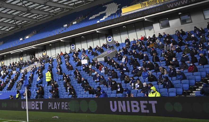 Fans, wearing a face mask, for covering due to the COVID-19 pandemic, sit socially distanced during the English Premier League soccer match between Brighton and Hove Albion and Sheffield United at the American Express Community Stadium in Brighton, England, Saturday, Dec. 20, 2020. (Glyn Kirk/Pool via AP)