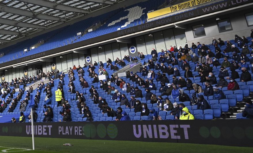 Fans, wearing a face mask, for covering due to the COVID-19 pandemic, sit socially distanced during the English Premier League soccer match between Brighton and Hove Albion and Sheffield United at the American Express Community Stadium in Brighton, England, Saturday, Dec. 20, 2020. (Glyn Kirk/Pool via AP)