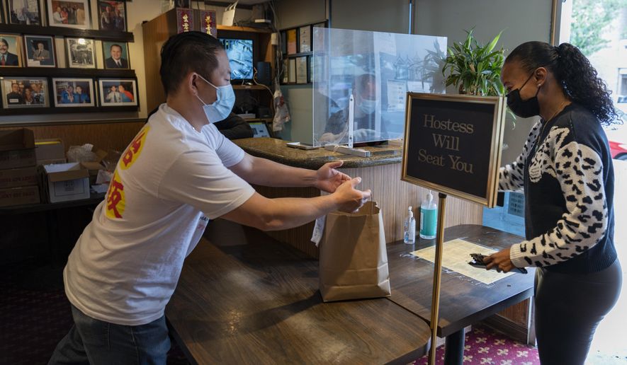 Benny Yun, owner of Yang Chow restaurant, left, delivers a take-out order in Los Angeles, Thursday, Dec. 17, 2020. Bigotry toward Asian Americans and Asian food has spread steadily alongside the coronavirus in the United States. Yun said even though his businesses have survived the pandemic, they get prank calls almost daily asking if they have dog or cat on the menu or impersonating a thick Asian accent. (AP Photo/Damian Dovarganes)