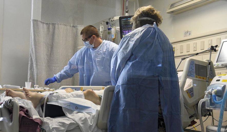 Nurse Jesse Phelps, left, works on a COVID-19 patient as a family member looks on at East Alabama Medical Center in the intensive care unit Thursday, Dec. 10, 2020, in Opelika, Ala. The medical center faces a new influx of COVID-19 patients as the pandemic intensifies. (AP Photo/Julie Bennett)