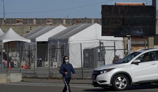 A pedestrian wears a face mask while walking past a car exiting the CityTestSF at Pier 30/32 COVID-19 testing site during the coronavirus pandemic in San Francisco, Wednesday, Dec. 23, 2020. (AP Photo/Jeff Chiu)