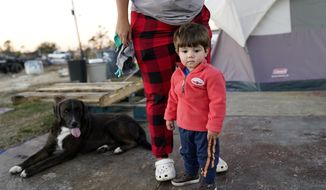 Katelyn Smith stands with her one year old son Ricky Trahan, III, as she prepares to change his clothes, as their family lives in a camper and tents where their home was destroyed, in the aftermath of Hurricane Laura and Hurricane Delta, in Lake Charles, La., Friday, Dec. 4, 2020. (AP Photo/Gerald Herbert)