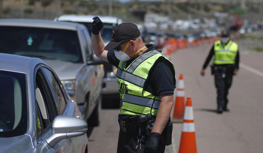FILE - In this May 7, 2020, file photo, New Mexico state police officers screen cars for compliance with an emergency lockdown order that bans nonessential visitors and limits vehicle passengers to two people as they enter Gallup, N.M. From lockdowns in tribal communities to the economic and social fallout reverberating through every facet of life in New Mexico, the coronavirus pandemic dominated headlines in 2020. COVID-19 infections were on track to top 140,000 by the end of the year, with the curve taking its steepest rise in November as part of what state health officials described as the third surge to hit New Mexico. (AP Photo/Morgan Lee, File)