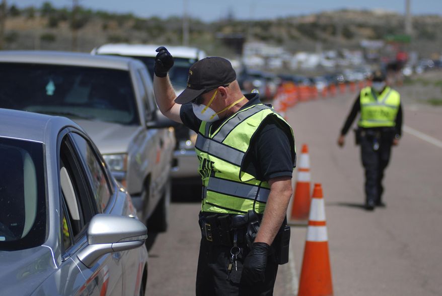 FILE - In this May 7, 2020, file photo, New Mexico state police officers screen cars for compliance with an emergency lockdown order that bans nonessential visitors and limits vehicle passengers to two people as they enter Gallup, N.M. From lockdowns in tribal communities to the economic and social fallout reverberating through every facet of life in New Mexico, the coronavirus pandemic dominated headlines in 2020. COVID-19 infections were on track to top 140,000 by the end of the year, with the curve taking its steepest rise in November as part of what state health officials described as the third surge to hit New Mexico. (AP Photo/Morgan Lee, File)