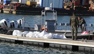 Tunisian coast guards stand next to the clovered dead bodies of migrants in the port of Sfax, central Tunisia, Thursday, Dec. 24, 2020. About 20 African migrants were found dead Thursday after their smuggling boat sank in the Mediterranean Sea while trying to reach Europe, Tunisian authorities said. Coast guard boats and local fishermen found and retrieved the bodies in the waters off the coastal city of Sfax in central Tunisia. (AP Photo/Houssem Zouari)