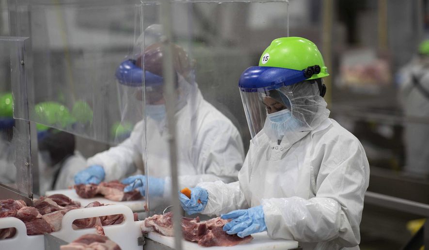 This May 20, 2020, photo provided by Smithfield Foods shows some of the measures the company says it has taken to limit the spread of the coronavirus inside its plants. Workers inside its Sioux Falls, South Dakota, pork processing plant wear protective gear and are separated by plastic partitions as they carve up meat. (Photo courtesy Smithfield Foods via AP)