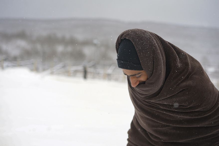 A migrant walks through the snow wrapped in a blanket at the Lipa camp northwestern Bosnia, near the border with Croatia, Saturday, Dec. 26, 2020. Hundreds of migrants are stranded in a burnt-out squalid camp in Bosnia as heavy snow fell in the country and temperatures dropped during a winter spell of bad weather after fire earlier this week destroyed much of the camp near the town of Bihac that already was harshly criticized by international officials and aid groups as inadequate for housing refugees and migrants.(AP Photo/Kemal Softic)
