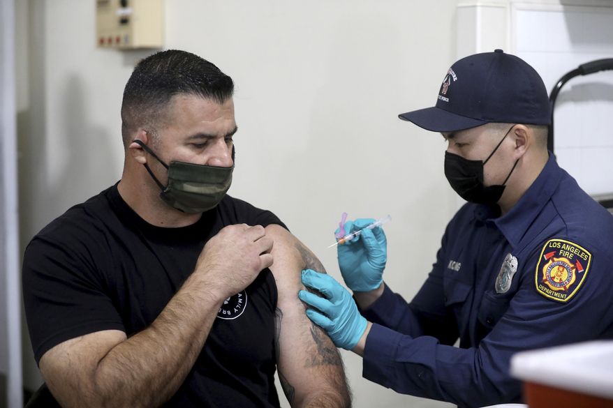 Los Angeles Fire Department Capt. Elliot Ibanez, left, receives the Moderna COVID-19 vaccine given by LAFD paramedic Anthony Kong at Station 4, Monday, Dec. 28, 2020, in Los Angeles. (Gary Coronado/Los Angeles Times via AP, Pool)