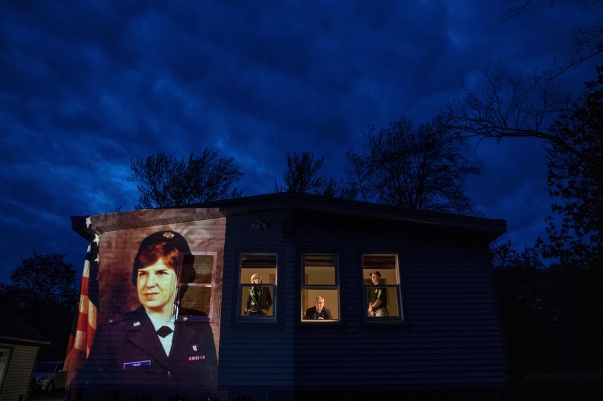 FILE - In this May 14, 2020, file photo, an image of veteran Constance "Kandy" Pinard is projected onto the home she grew up in with her sister, Tammy Petrowicz, left, and brothers, Paul, center, and Brian Driscoll in Florence, Mass. Pinard, a nurse in the U.S. Air Force and resident of the Soldier's Home in Holyoke, Mass., died from the COVID-19 virus at the age of 73. The coronavirus pandemic was Massachusetts' top story of 2020. (AP Photo/David Goldman, File)