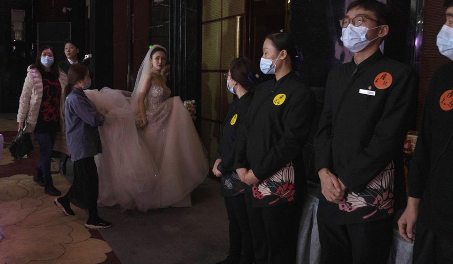 Bride Chen Yaxuan walks by staff wearing masks during a wedding banquet in Beijing on Saturday, Dec. 12, 2020. Lovebirds in China are embracing a sense of normalcy as the COVID pandemic appears to be under control in the country where it was first detected. (AP Photo/Ng Han Guan)