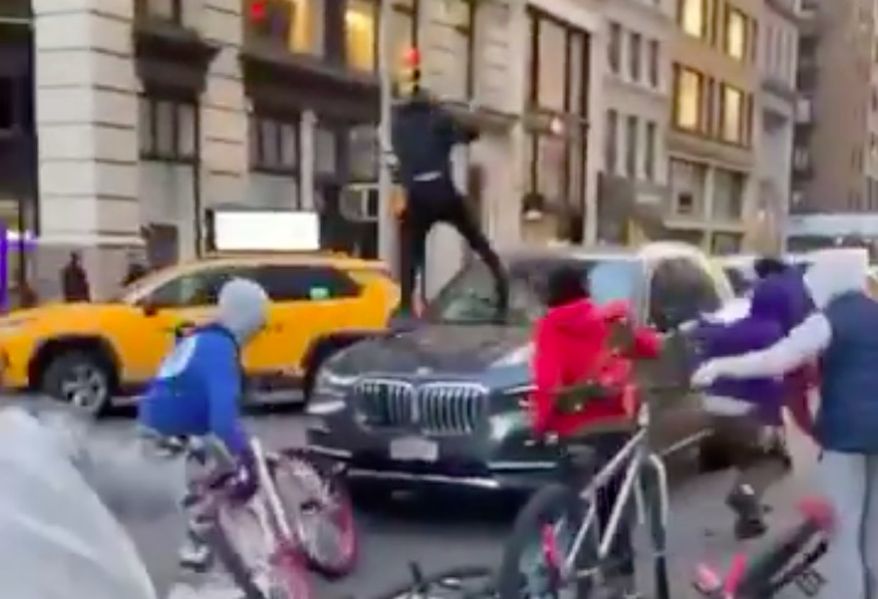 A group of teenagers on bikes attacked a BMW with two people inside in broad daylight in New York City Tuesday, multiple videos show. (Screenshot via Twitter/@GrantB911)