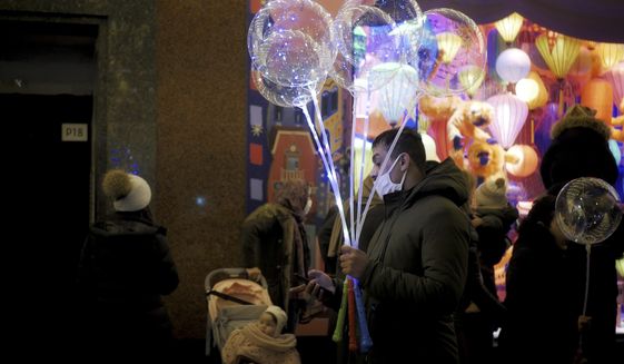A man holds light balloons as he checks his phone on a sidewalk next to a department store in Paris, Thursday, Dec. 31, 2020. (AP Photo/Thibault Camus)