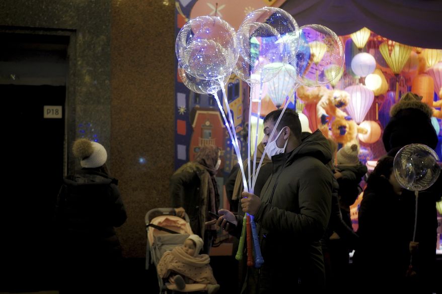A man holds light balloons as he checks his phone on a sidewalk next to a department store in Paris, Thursday, Dec. 31, 2020. (AP Photo/Thibault Camus)
