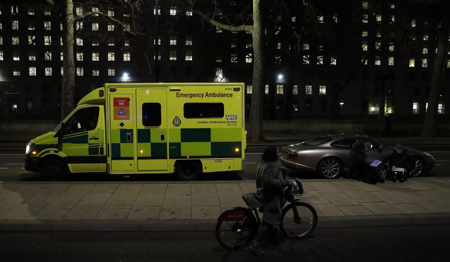 A woman with a bicycle walks past an ambulance and members of the media on the north bank of the River Thames opposite the London Eye ferris wheel by the River Thames in London, Thursday, Dec. 31, 2020. The London Eye is one of the traditional sites for New Year's Eve firework display, but it has been cancelled due to the ongoing coronavirus pandemic and the restrictions in place to try and stop its spread. (AP Photo/Matt Dunham)