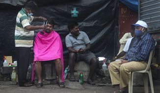 A roadside barber wearing mask as a precaution against the coronavirus gives hair cut to a man as others wait for their turn in Mumbai, India, Sunday, Jan. 3, 2021. India authorized two COVID-19 vaccines on Sunday, paving the way for a huge inoculation program to stem the coronavirus pandemic in the world’s second most populous country. (AP Photo/Rafiq Maqbool)