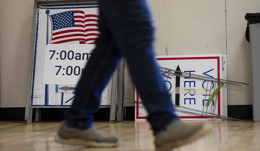 A worker passes voting signs while setting up a polling location at an elementary school in Gwinnett County, Ga., outside of Atlanta on Monday, Jan. 4, 2021, in advance of the Senate runoff election. (AP Photo/Ben Gray)