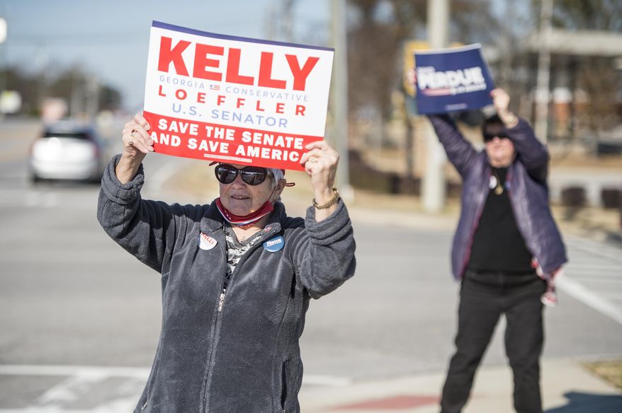 Jean Calvert, left, and Debbie Epling wave signs for their favorite candidates at the intersection Belair and Washington Roads during Georgia's U.S. Senate runoff election in Evans, Ga., Tuesday morning, Jan. 5, 2021. Republican Sen. Kelly Loeffler and David Perdue are being challenged by Democrats Jon Ossoff and Raphael Warnock in Tuesday's runoff. (Michael Holahan/The Augusta Chronicle via AP)