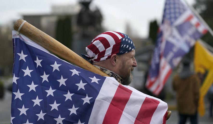 A man carries a U.S. flag attached to a baseball bat as he waits at the Capitol in Olympia, Wash., Wednesday, Jan. 6, 2021, before the start of a protest rally against the counting of electoral votes in Washington, DC, affirming President-elect Joe Biden's victory. People supporting President Donald Trump and other supporters began arriving at the Capitol mid-morning for a protest rally Wednesday that was expected to begin at noon. (AP Photo/Ted S. Warren)