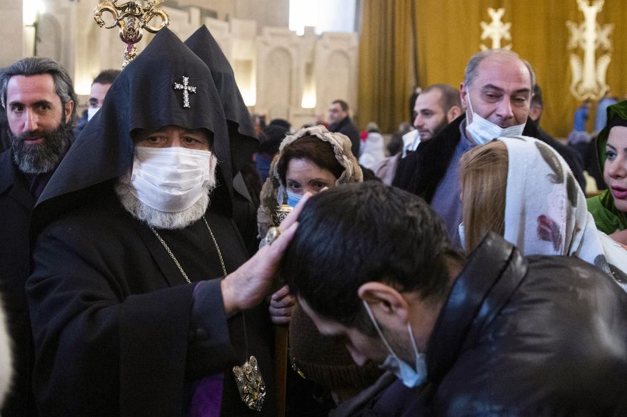 Armenian Catholicos Karekin II wearing a face mask to protect against coronavirus, left, blesses a believer after the Christmas Mass in the Saint Gregory the Illuminator Cathedral in Yerevan, Armenia, Wednesday, Jan. 6, 2021. Armenia's prime minister, who is under harsh criticism from the country's dominant Orthodox Christian church in connection with the recent war with Azerbaijan, stayed away from Christmas services on Wednesday. Orthodox Christians celebrate Christmas on Jan. 7, in accordance with the Julian calendar. (Grigor Yepremyan/PAN Photo via AP)