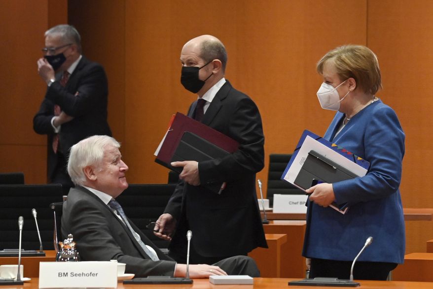 German Chancellor Angela Merkel walks beside Federal Finance Minister Olaf Scholz and Interior Minister Horst Seehofer, from right, prior the weekly cabinet meeting on Wednesday, Jan. 6, 2021 at the Chancellery in Berlin, Germany. (John MacDougall/Pool via AP)