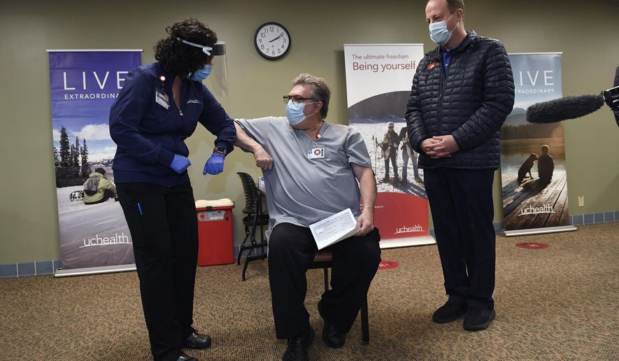 With Gov. Jared Polis, right, watching, Christy Ruffell, left, manager of clinic nursing standards at UCHealth Medical Center, gives an elbow-bump to Kevin Londrigan, center, a respiratory therapist at UCHealth Medical Center,  before giving him the very first dose of the Covid-19 vaccine in Colorado at UCHealth Poudre Valley Hospital, Monday, Dec. 14, 2020, in Fort Collins, Colo. (Helen H. Richardson/The Denver Post via AP)