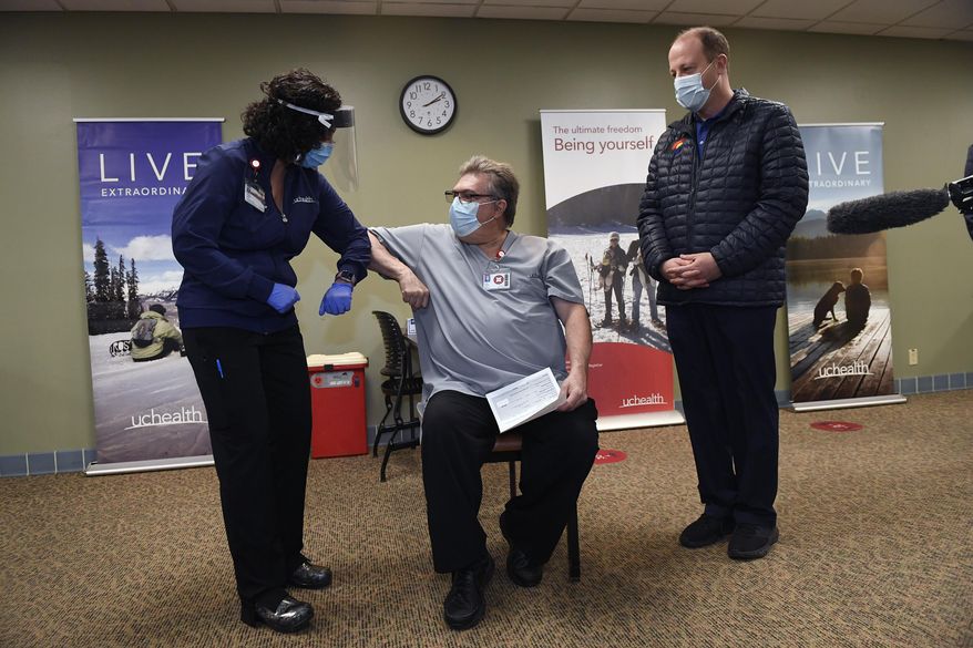 With Gov. Jared Polis, right, watching, Christy Ruffell, left, manager of clinic nursing standards at UCHealth Medical Center, gives an elbow-bump to Kevin Londrigan, center, a respiratory therapist at UCHealth Medical Center,  before giving him the very first dose of the Covid-19 vaccine in Colorado at UCHealth Poudre Valley Hospital, Monday, Dec. 14, 2020, in Fort Collins, Colo. (Helen H. Richardson/The Denver Post via AP)