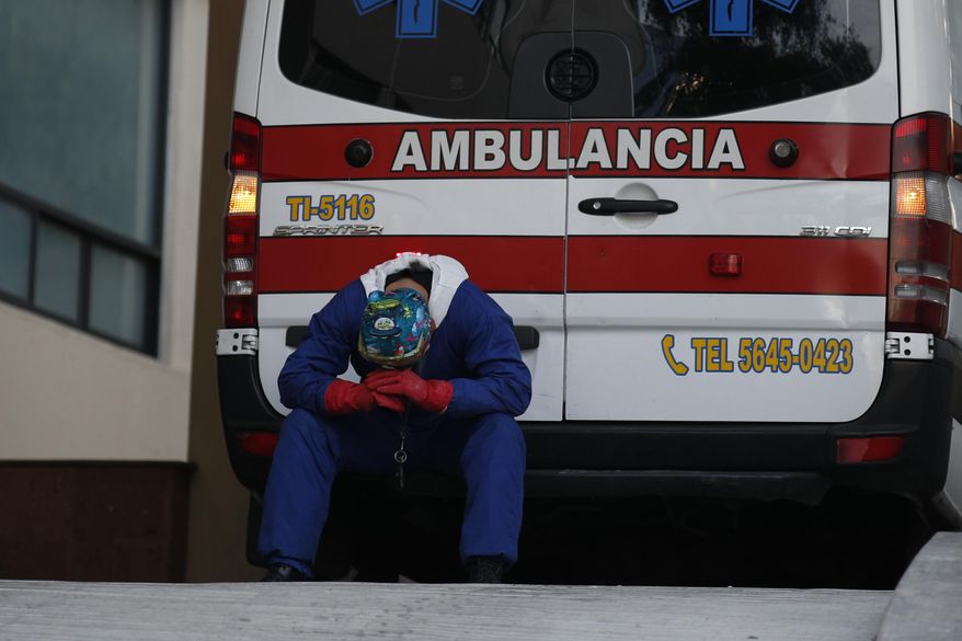 A paramedic rests behind his ambulance, as ambulance staff wait hours for the COVID-19 patients they are transporting to be admitted, at Siglo XXI Medical Center in Mexico City, Thursday, Jan. 7, 2021. A line of five ambulances spent hours outside the hospital Thursday afternoon waiting for their patients to be admitted, as hospitals in the capital near full capacity amid an unprecedented surge in coronavirus cases in Mexico.(AP Photo/Rebecca Blackwell)