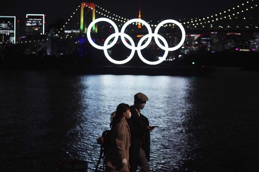 In this Dec. 1, 2020, file photo, a man and a woman walk past near the Olympic rings floating in the water in the Odaiba section in Tokyo. More than 80% of people in Japan who were surveyed in two polls in the last few days say the Tokyo Olympics should be canceled or postponed, or say they believe the Olympics will not take place. (AP Photo/Eugene Hoshiko, File)