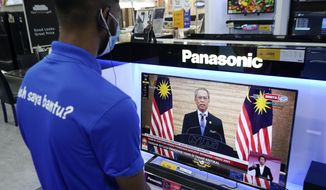 An electronic shop worker wearing a face mask watches a live broadcast of Malaysian Prime Minister Muhyiddin Yassin at a shopping outlet in Kuala Lumpur, Malaysia, Tuesday, Jan. 12, 2021. Malaysia&#39;s king Tuesday approved a coronavirus emergency that will prorogue parliament and halt any bids to seek a general election in a political reprieve for embattled Muhyiddin. (AP Photo/Vincent Thian)