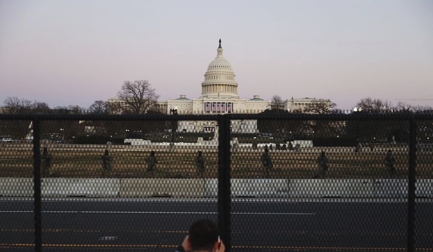 A person takes a view of the U.S. Capitol Wednesday, Jan. 13, 2021, from behind a security fence that was erected to reinforce security at the Capitol in Washington. (AP Photo/Shafkat Anowar)