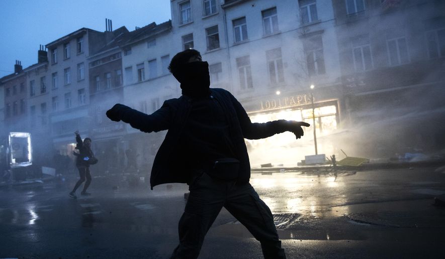 A protestor throws stones toward police officers in the Belgium capital, Brussels, Wednesday, Jan. 13, 2021, at the end of a protest asking for authorities to shed light on the circumstances surrounding the death of a 23-year-old Black man who was detained by police last week in Brussels. The demonstration in downtown Brussels was largely peaceful but was marred by incidents sparked by rioters who threw projectiles at police forces and set fires before it was dispersed. (AP Photo/Francisco Seco)